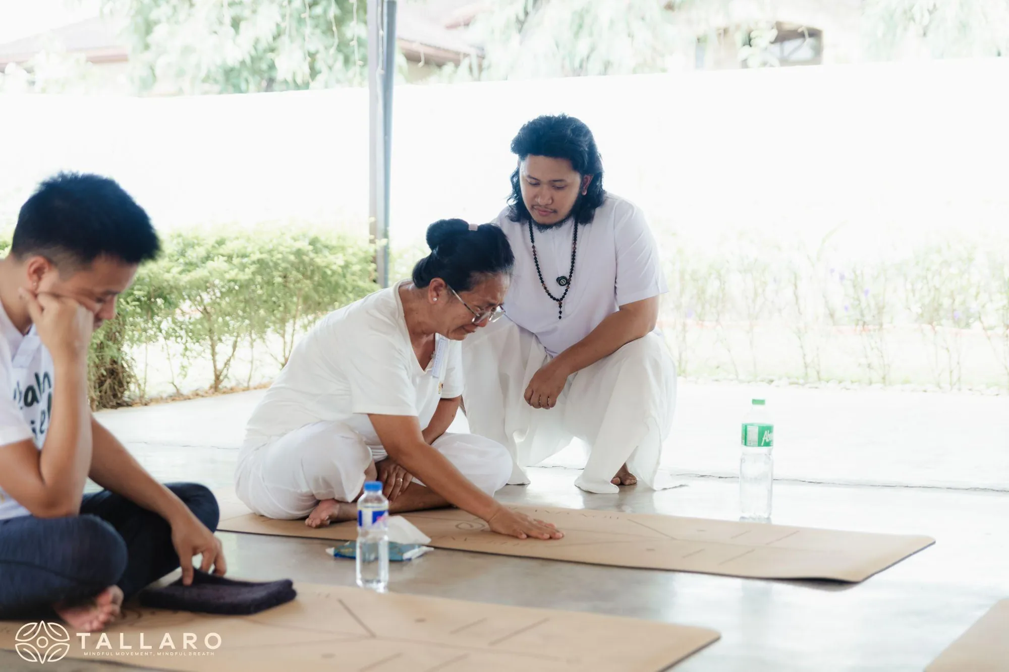 Teacher Ian kneeling on a mat beside a participant, gently guiding her during a session