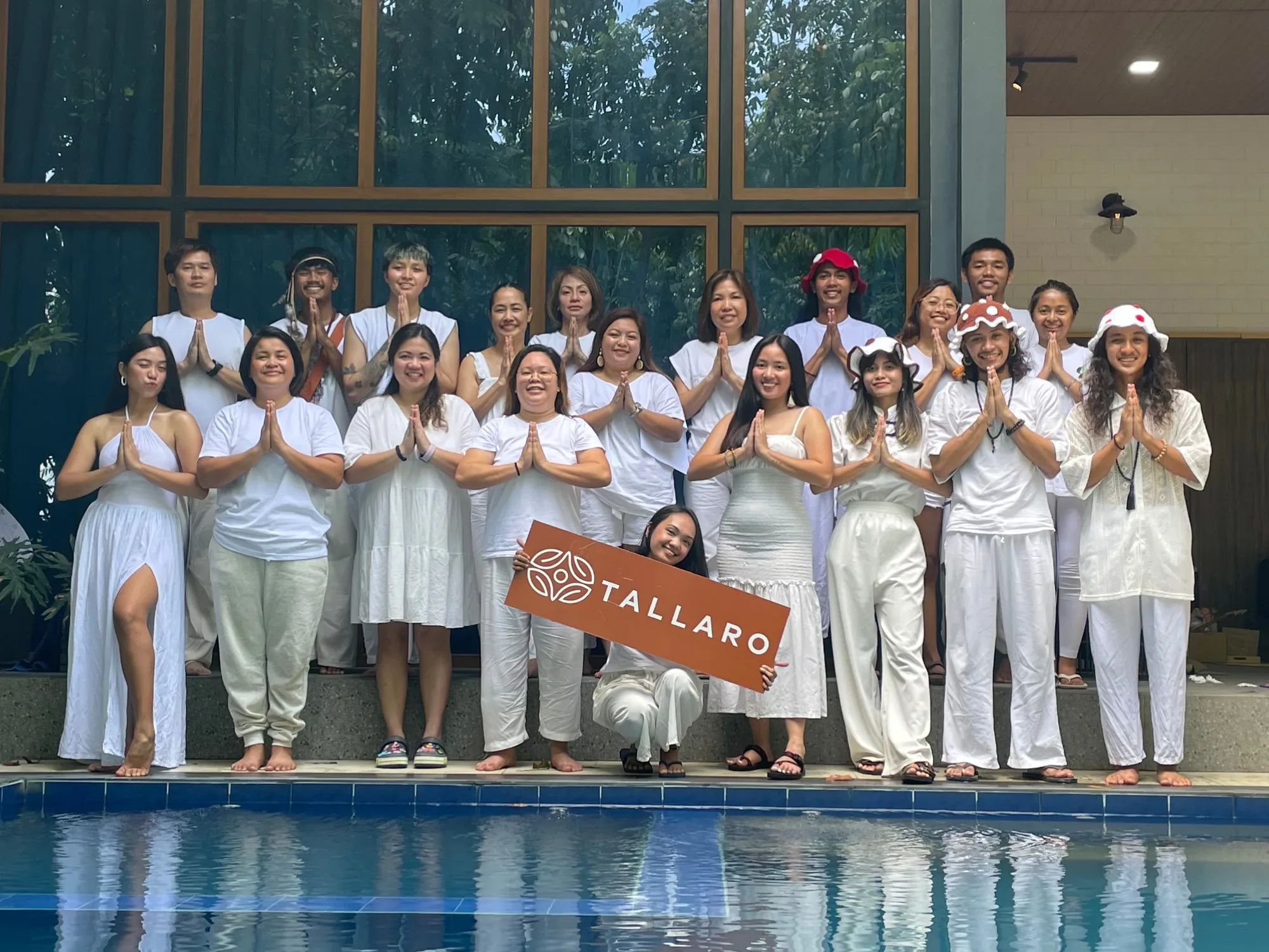 A Tallaro group in white smiling together by the pool, holding up a Tallaro sign