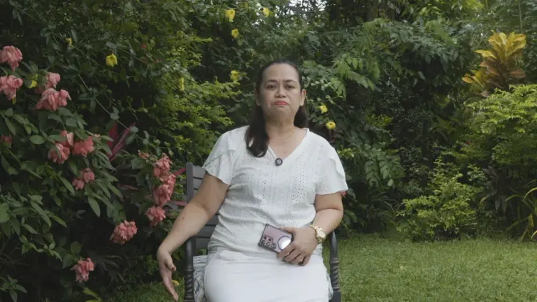 Dimple Reyes seated in a flowering garden during her recorded reflection.