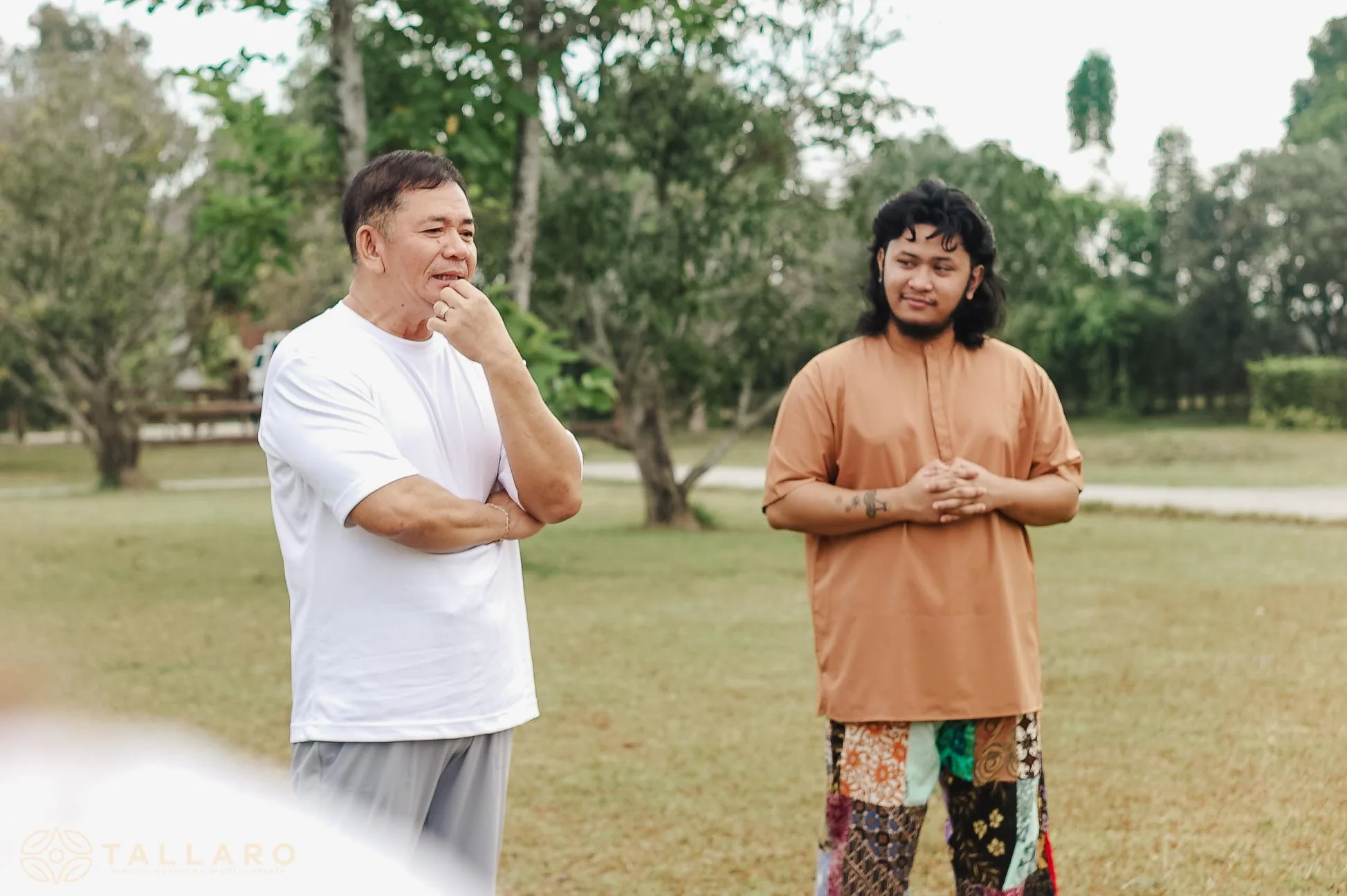 Teacher Ian in conversation with a participant on an open field, both listening thoughtfully